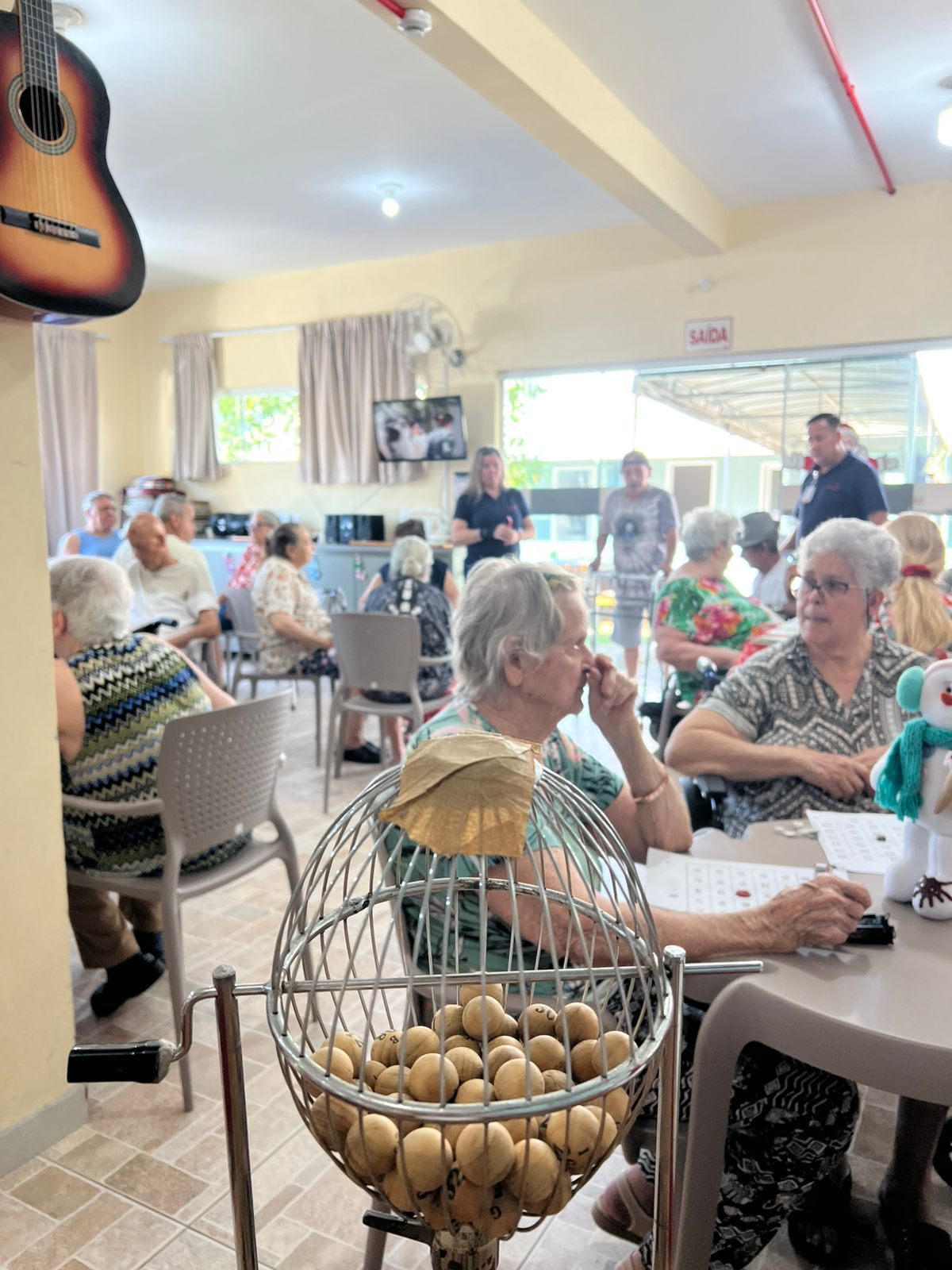 Salão do Asilo Dom Bosco durante o bingo solidário, com moradores reunidos nas mesas