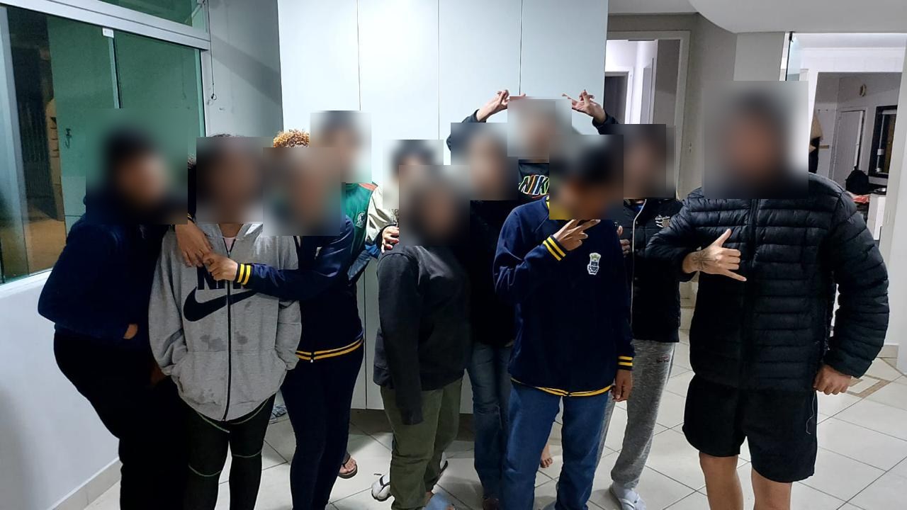 Grupo de adolescentes reunido no lar de acolhimento com voluntário, com rostos desfocados para preservar a identidade