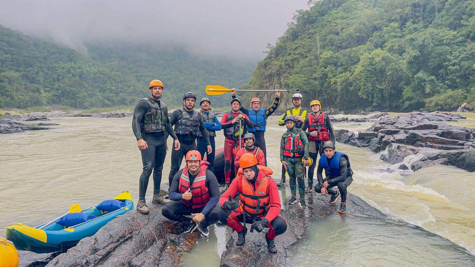 Turma do curso de resgate em águas rápidas reunida sobre as pedras do rio, com botes e equipamentos
