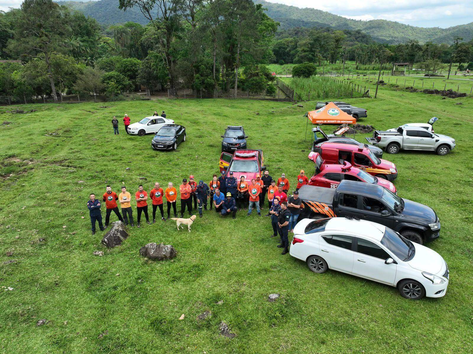 Vista aérea da equipe de voluntários reunida ao lado das viaturas e da tenda do Grupo de Resgate em Montanha